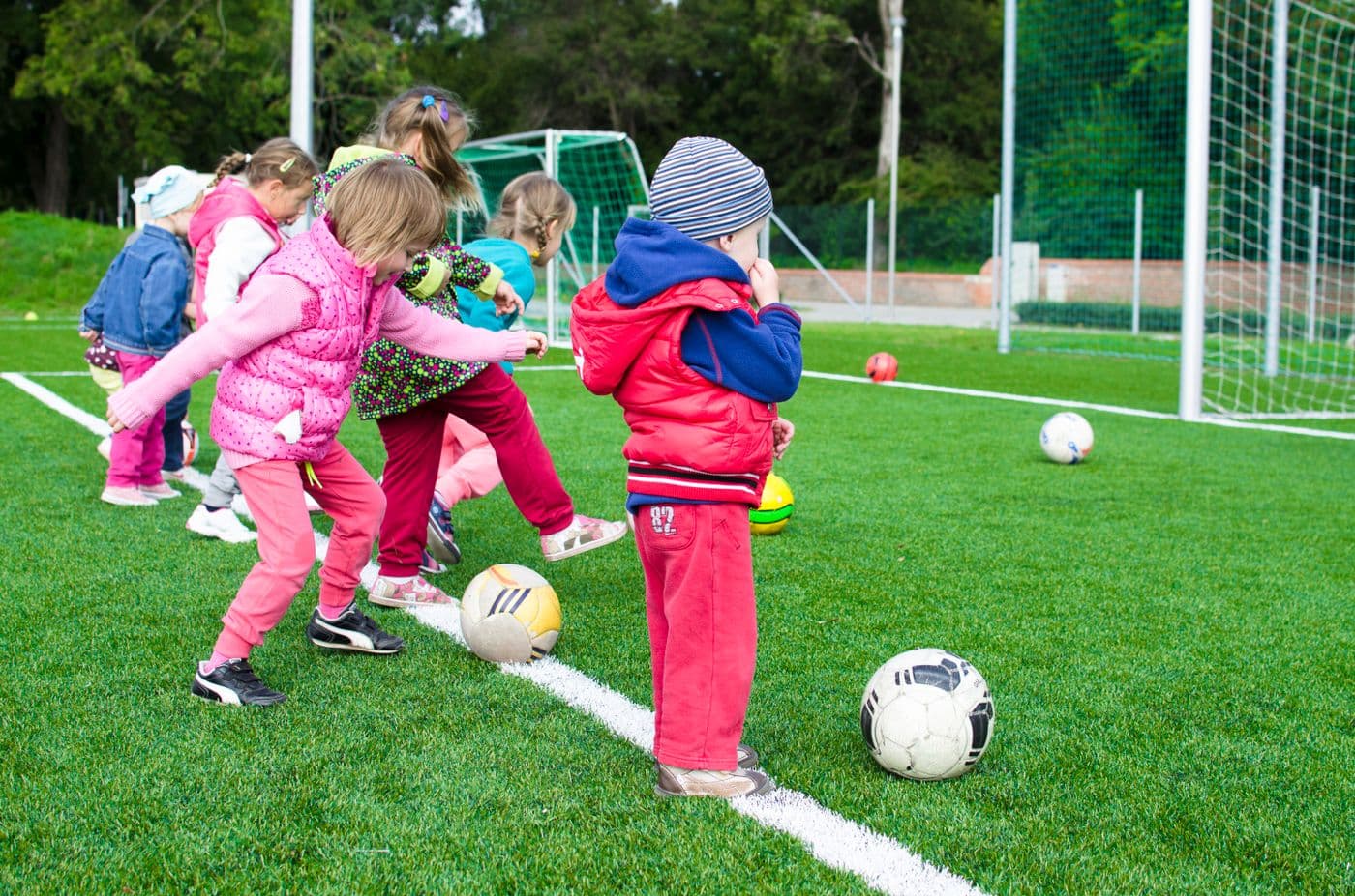 Young children in winter coats dribbling footballs across a cold training pitch